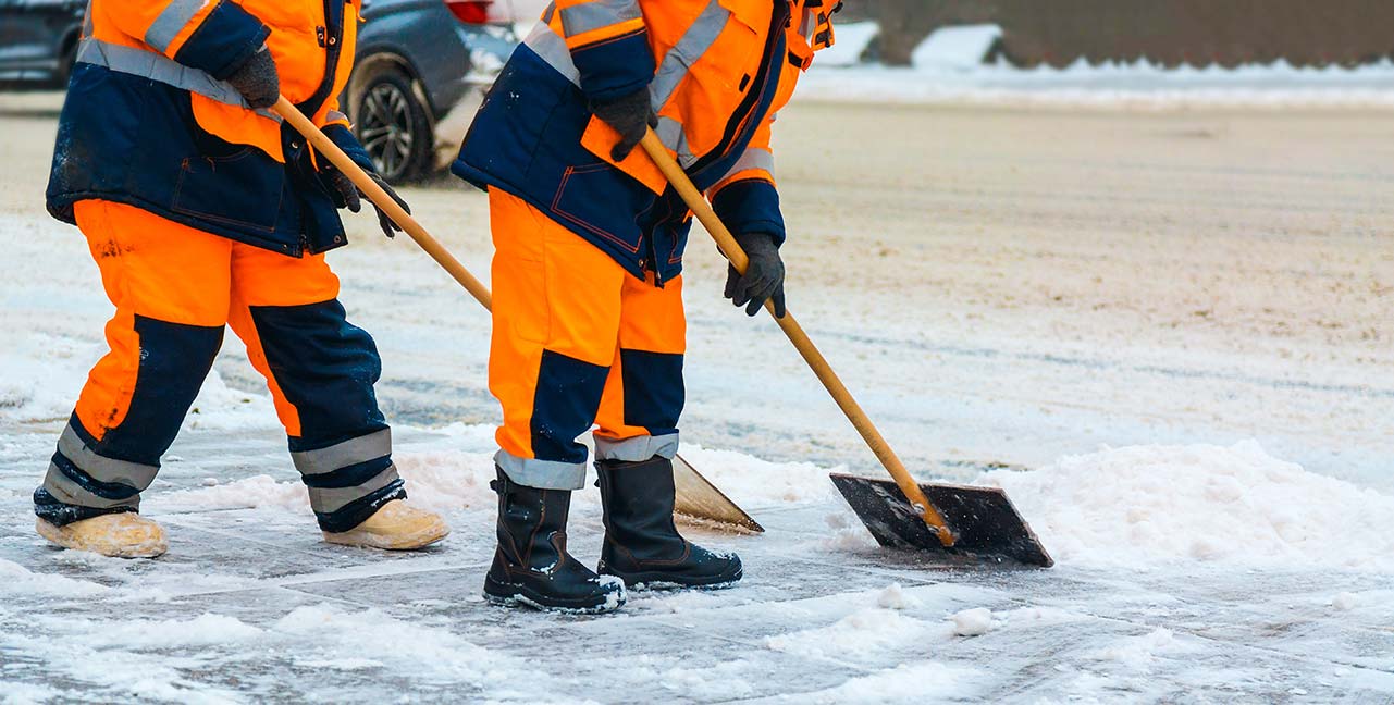 Two man in orange and blue uniform shovelling snow in Midland
